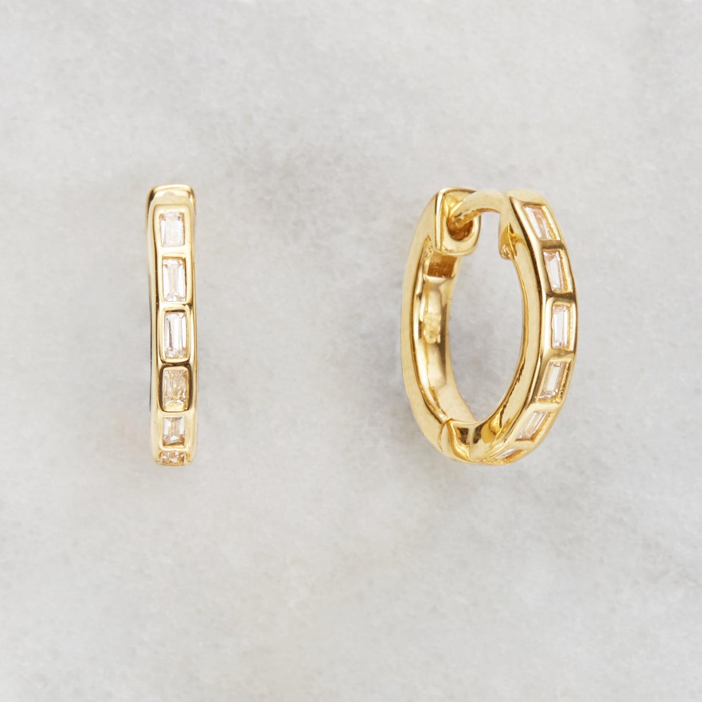 Gold diamond style baguette medium hoop earrings on a marble background
