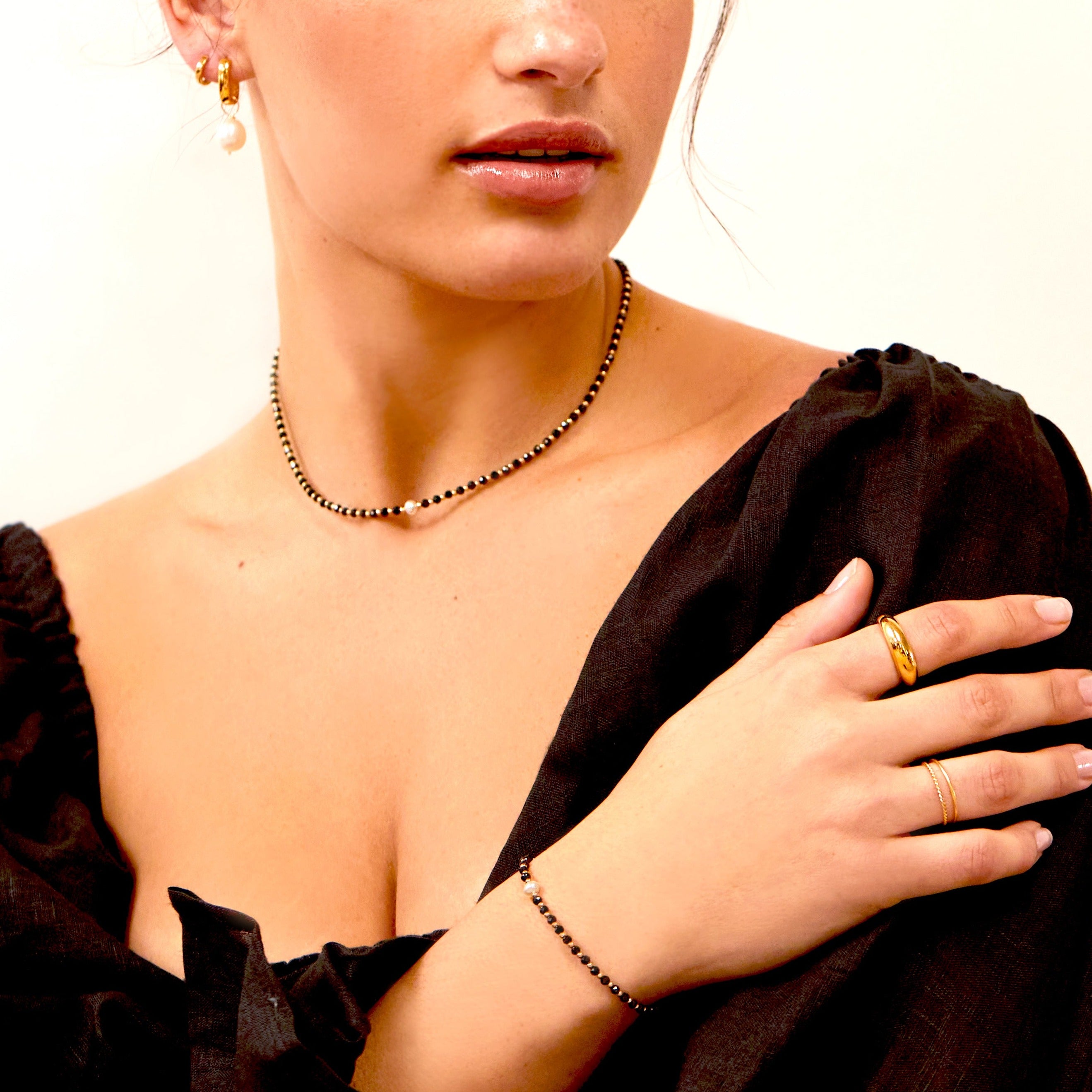 Gold spinel gemstone bracelet on a wrist and gold spinel gemstone choker around the neck of a woman wearing a black puffy sleeves and a gold plain dome ring on her finger