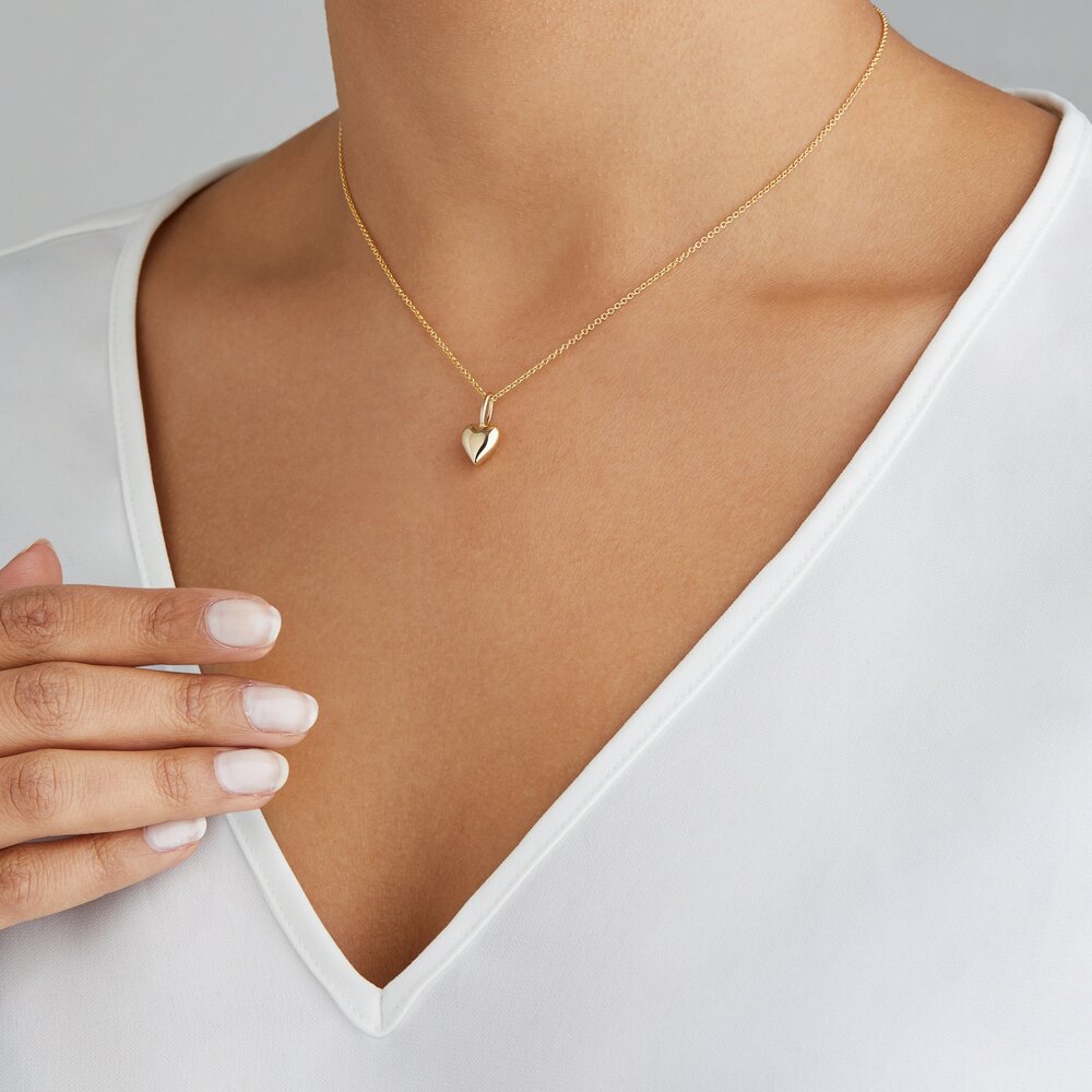 Gold heart pendant necklace around neck with white v neck top