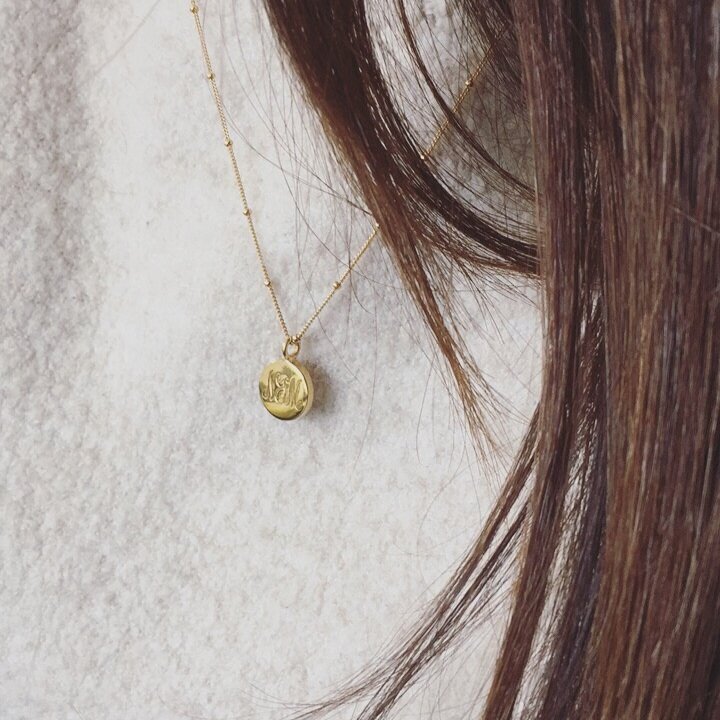 Gold large engraved disc necklace worn on top of a grey jumper of a brunette woman
