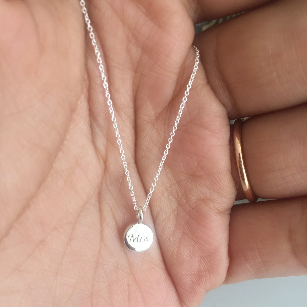 Silver extra small personalised Mrs disc necklace around neck with a white V neck top