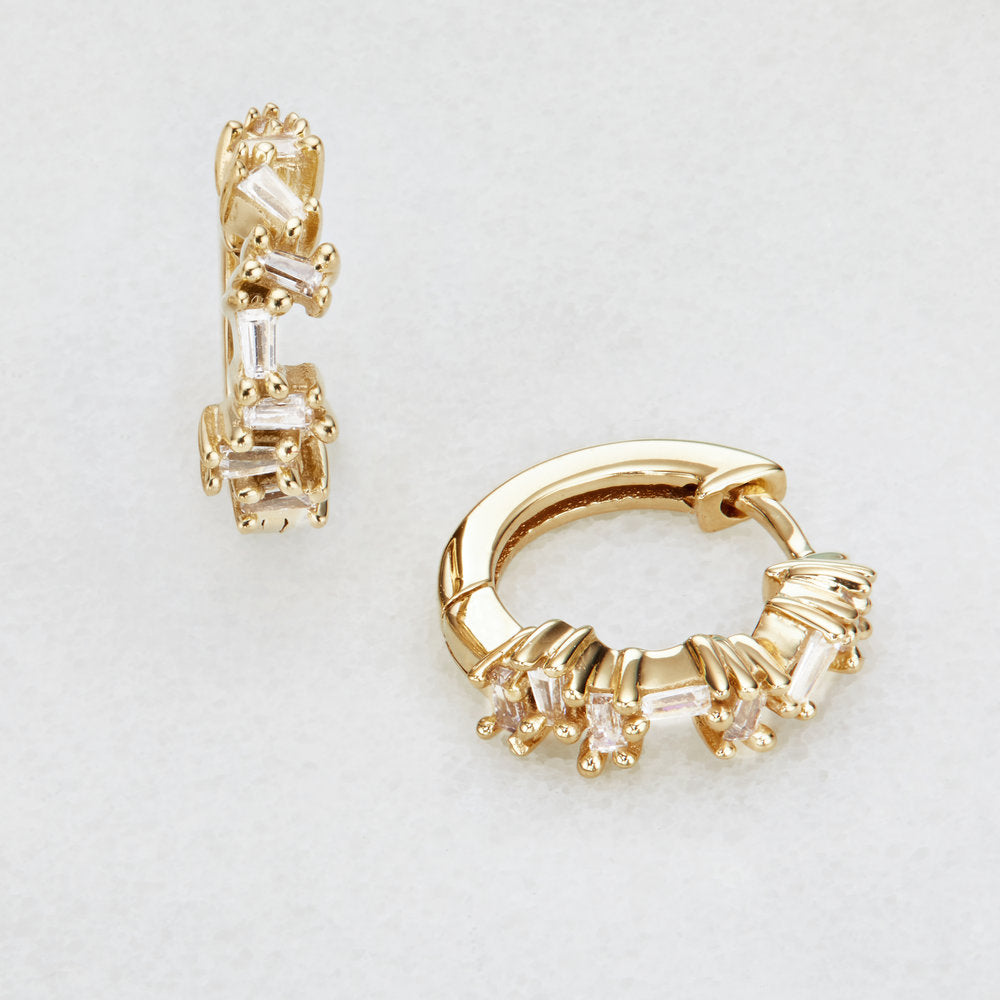 Gold diamond style jagged huggie hoop earrings on a white surface