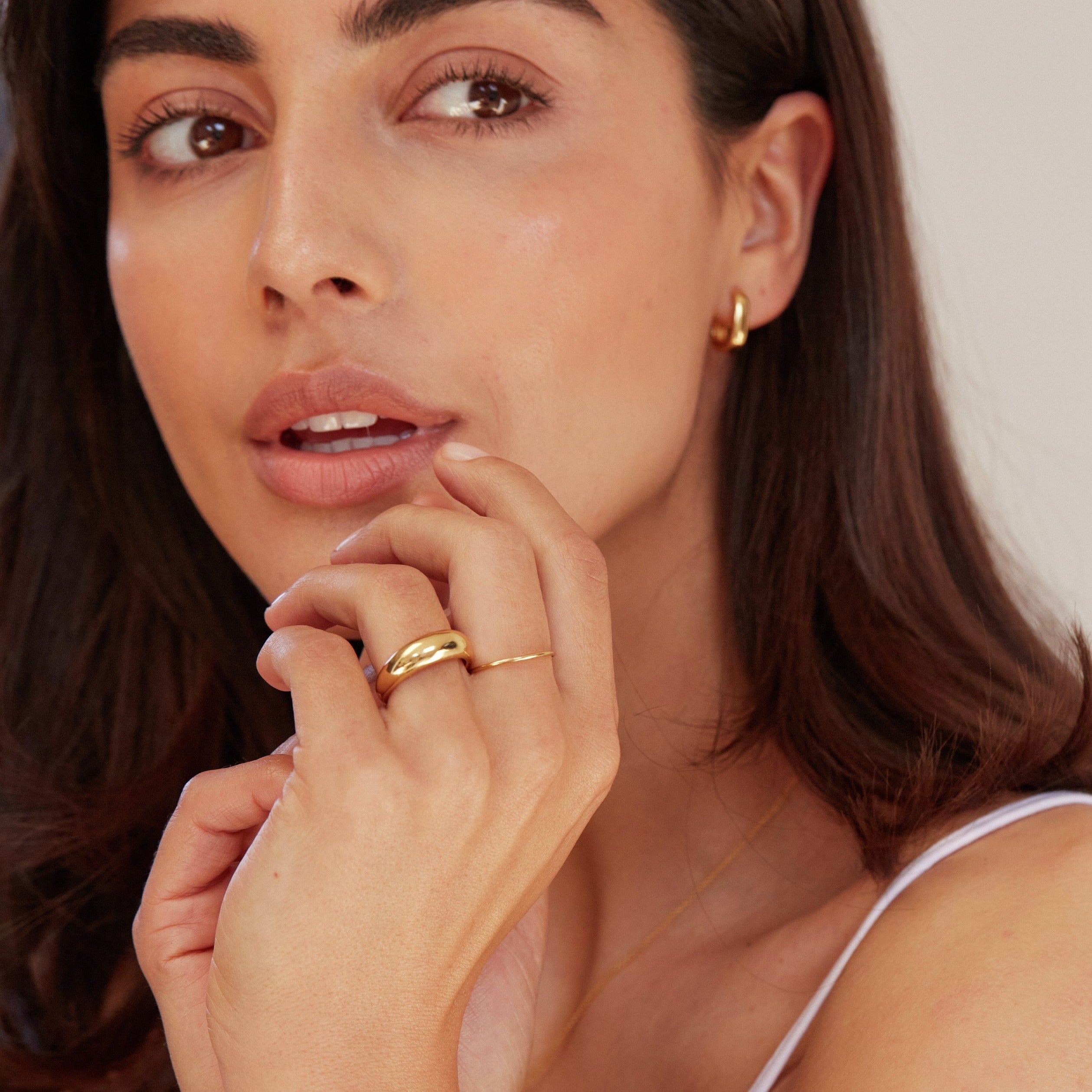 Gold thin plain stacking ring and a gold plain dome ring on a brunette woman's hand placed just under her lips with her mouth slighlty open