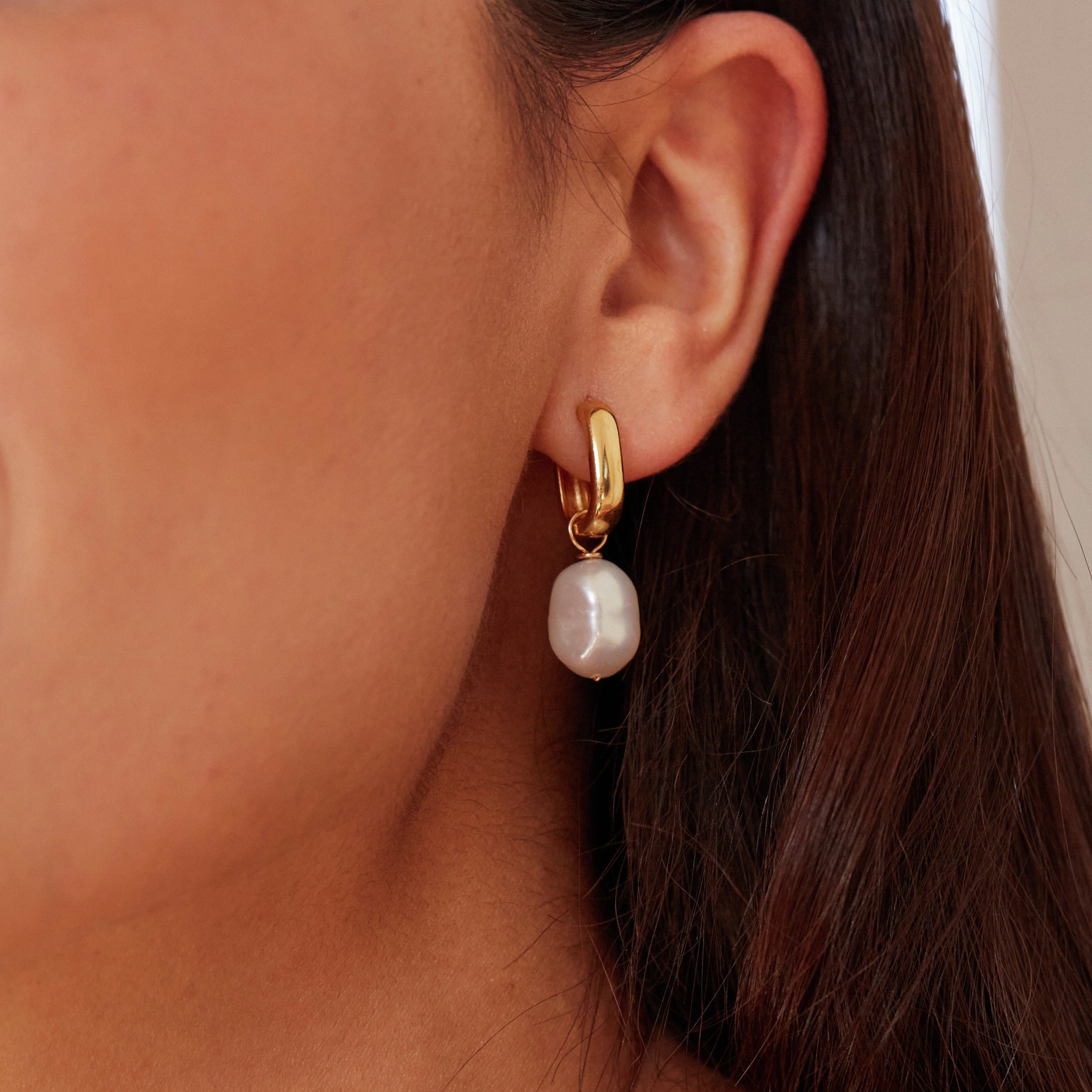 Gold thick squared hoop pearl drop earring in one ear lobe of a brunette woman
