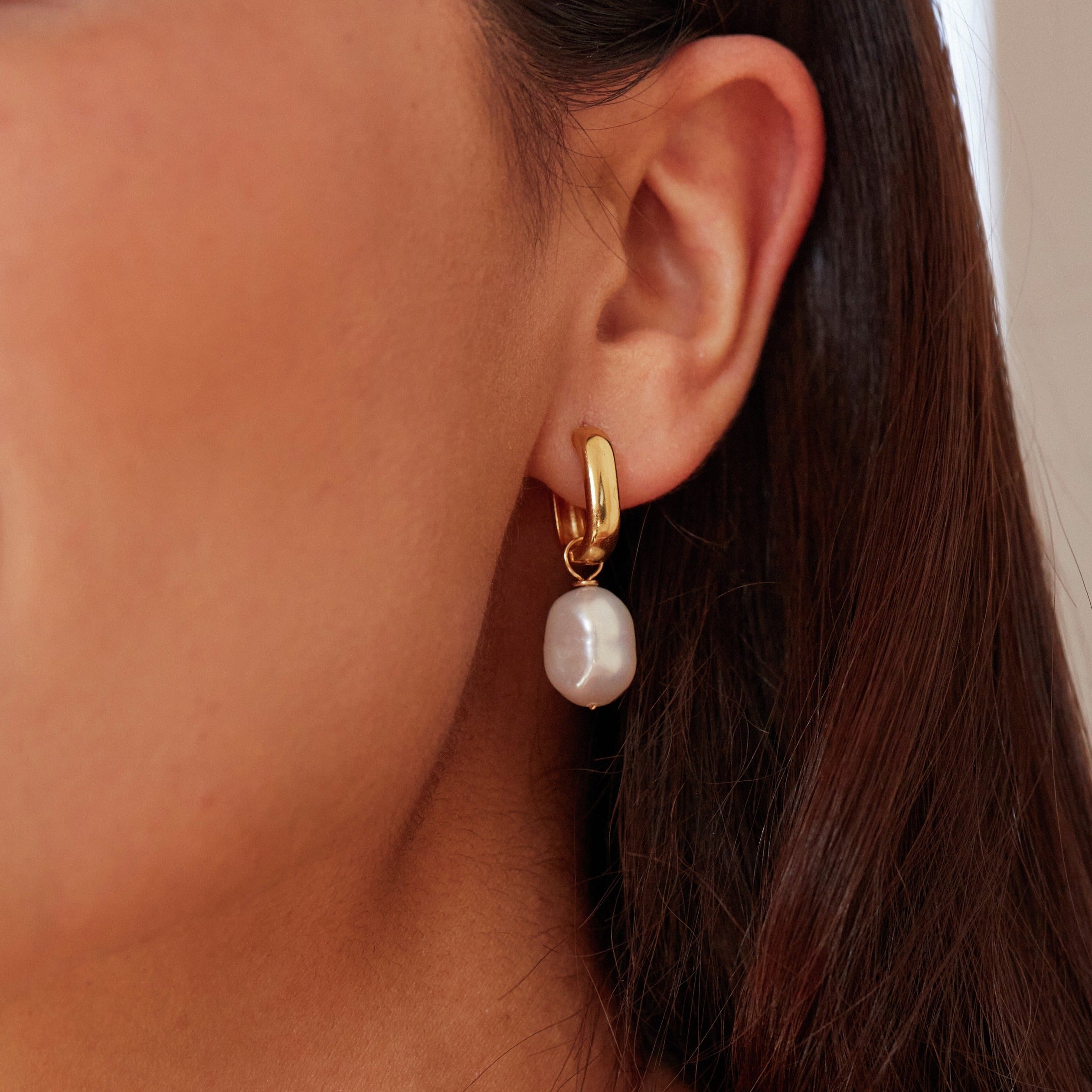 A gold thick squared hoop pearl drop earring close up in an ear lobe