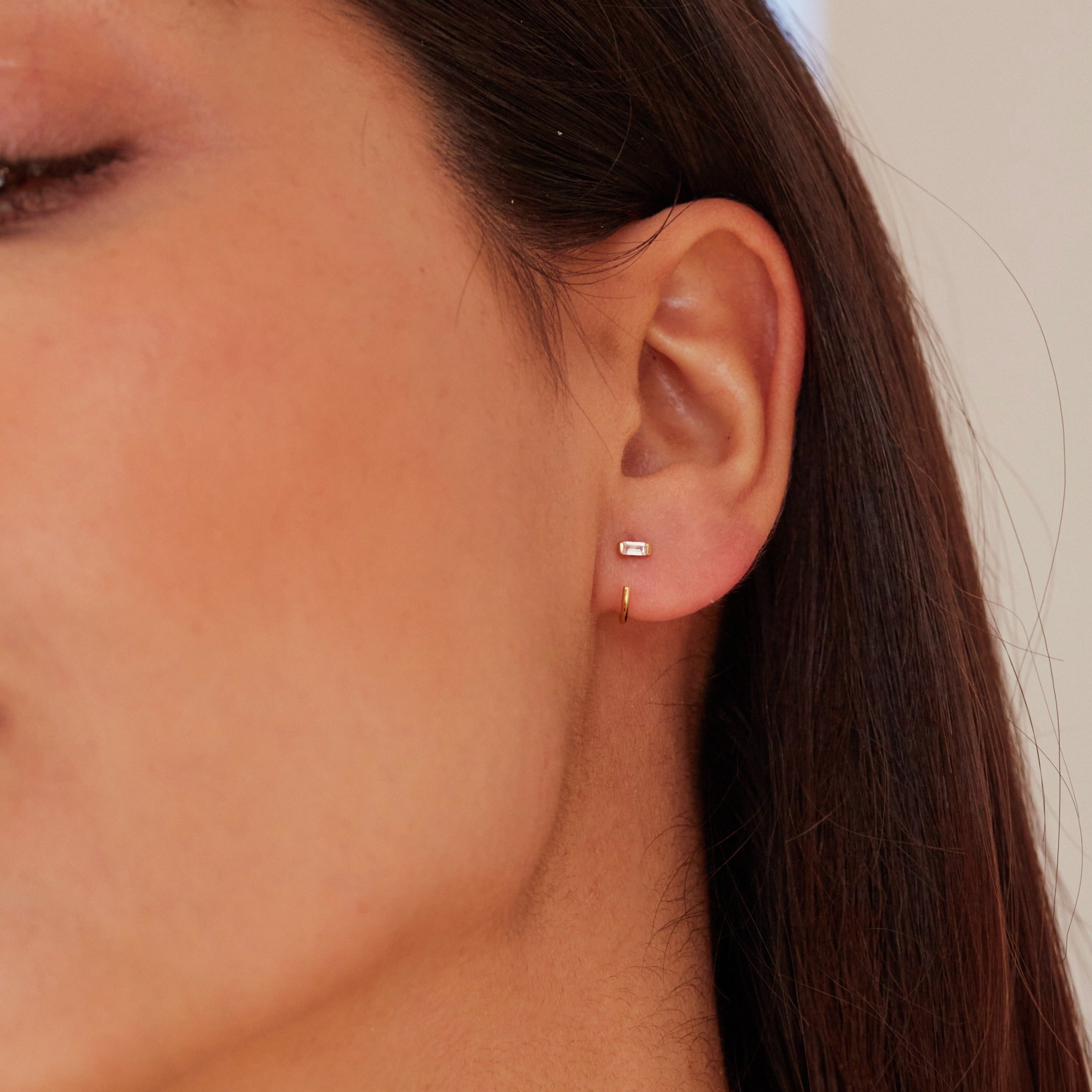 Gold diamond style baguette lobe hoop earring in one ear lobe of a brunette woman