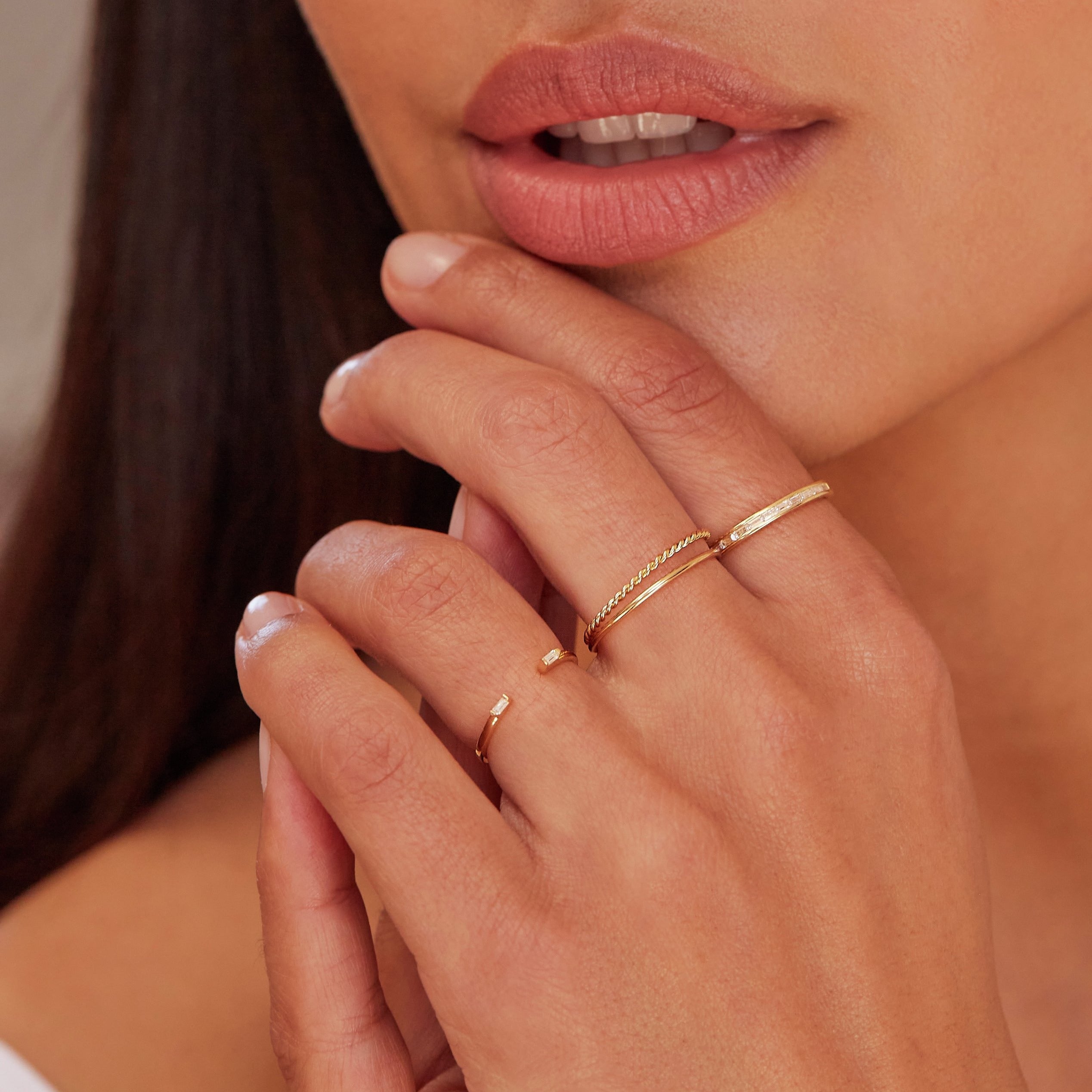 Gold thin plain stacking ring and a gold thin twisted stacking ring stacked on one finger with a gold diamond style baguette gap ring on another finger and a gold diamond style baguette eternity ring on another finger