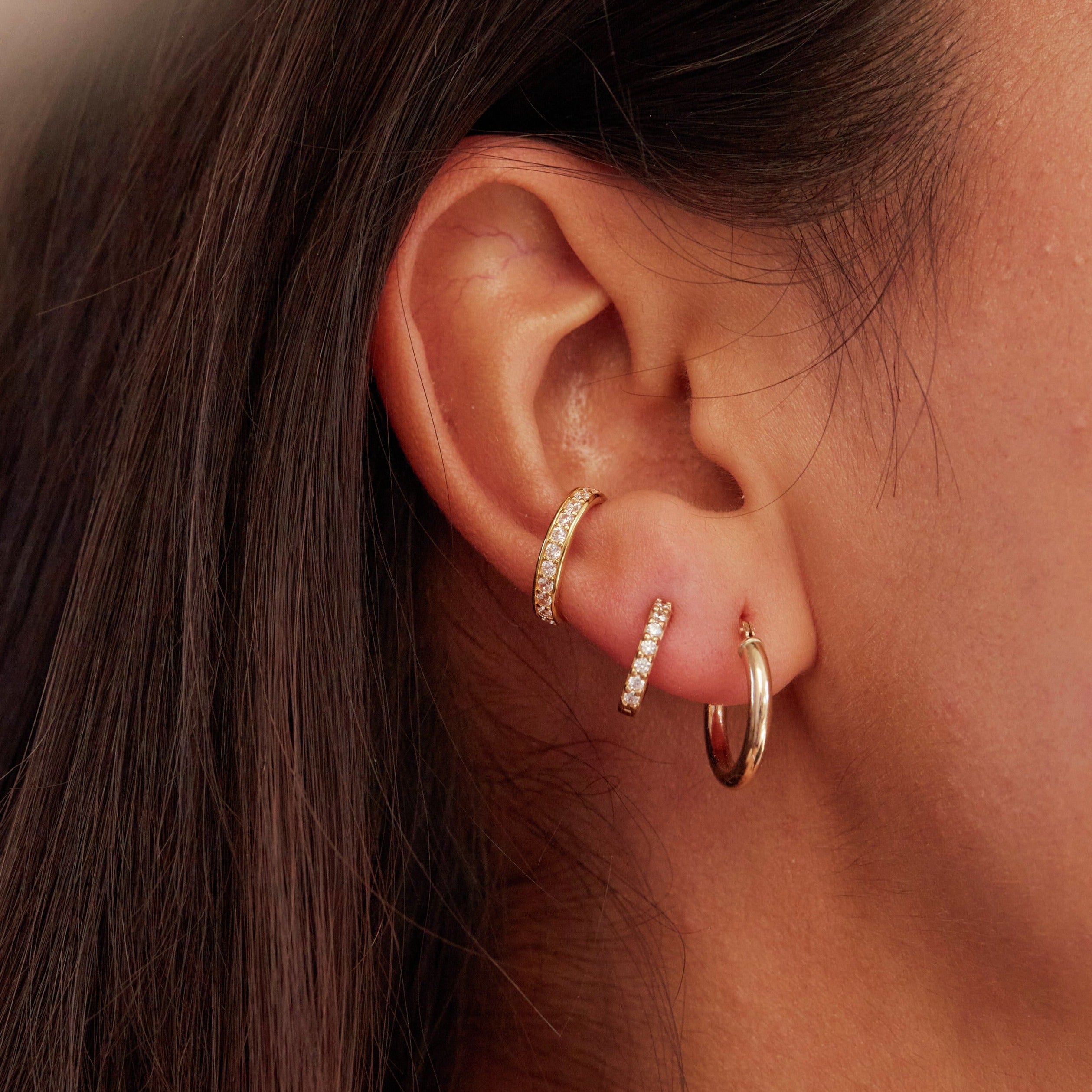 Gold diamond style huggie hoop earrings with other huggie hoop earrings in one ear lobe