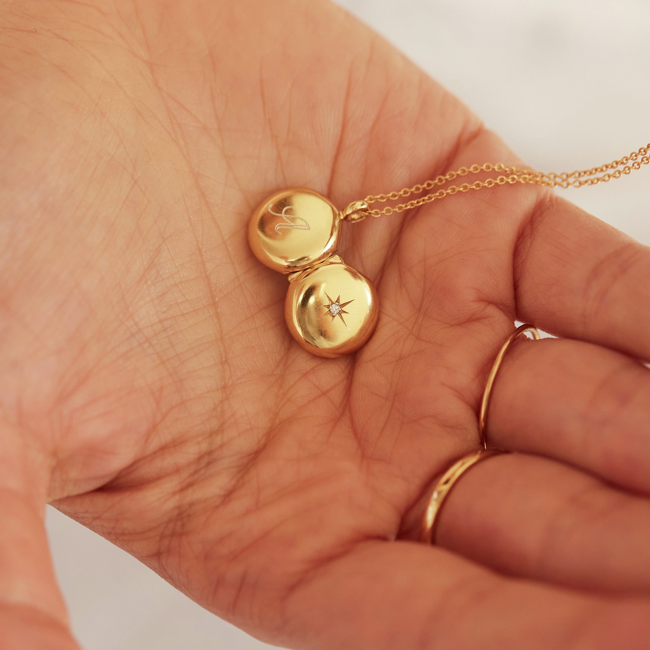 Open gold small round diamond locket necklace facing into the palm of a hand with the letter 'A' engraved