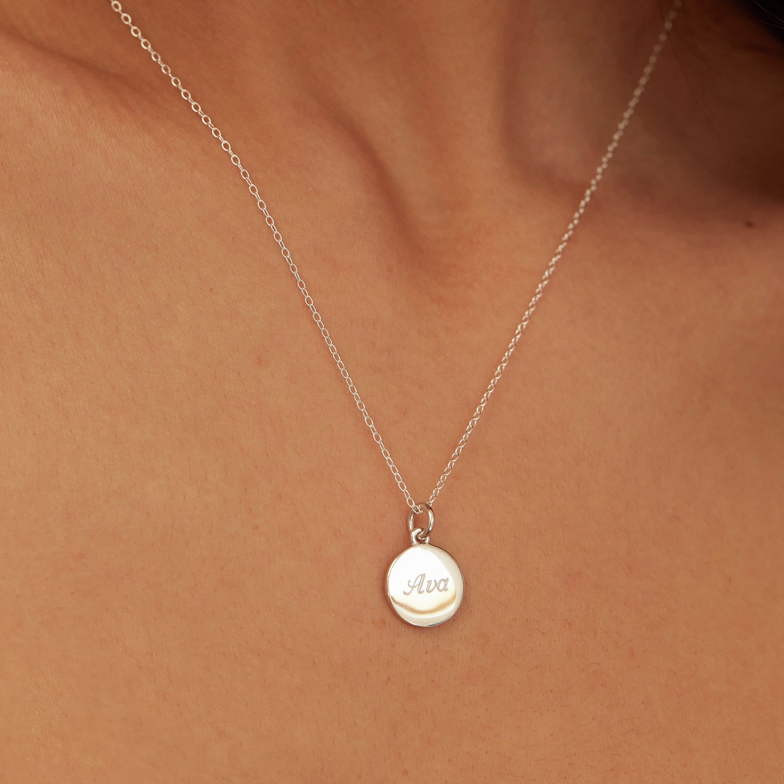 A silver small round engraved disc necklace with the name 'Ava' engraved close up on a chest