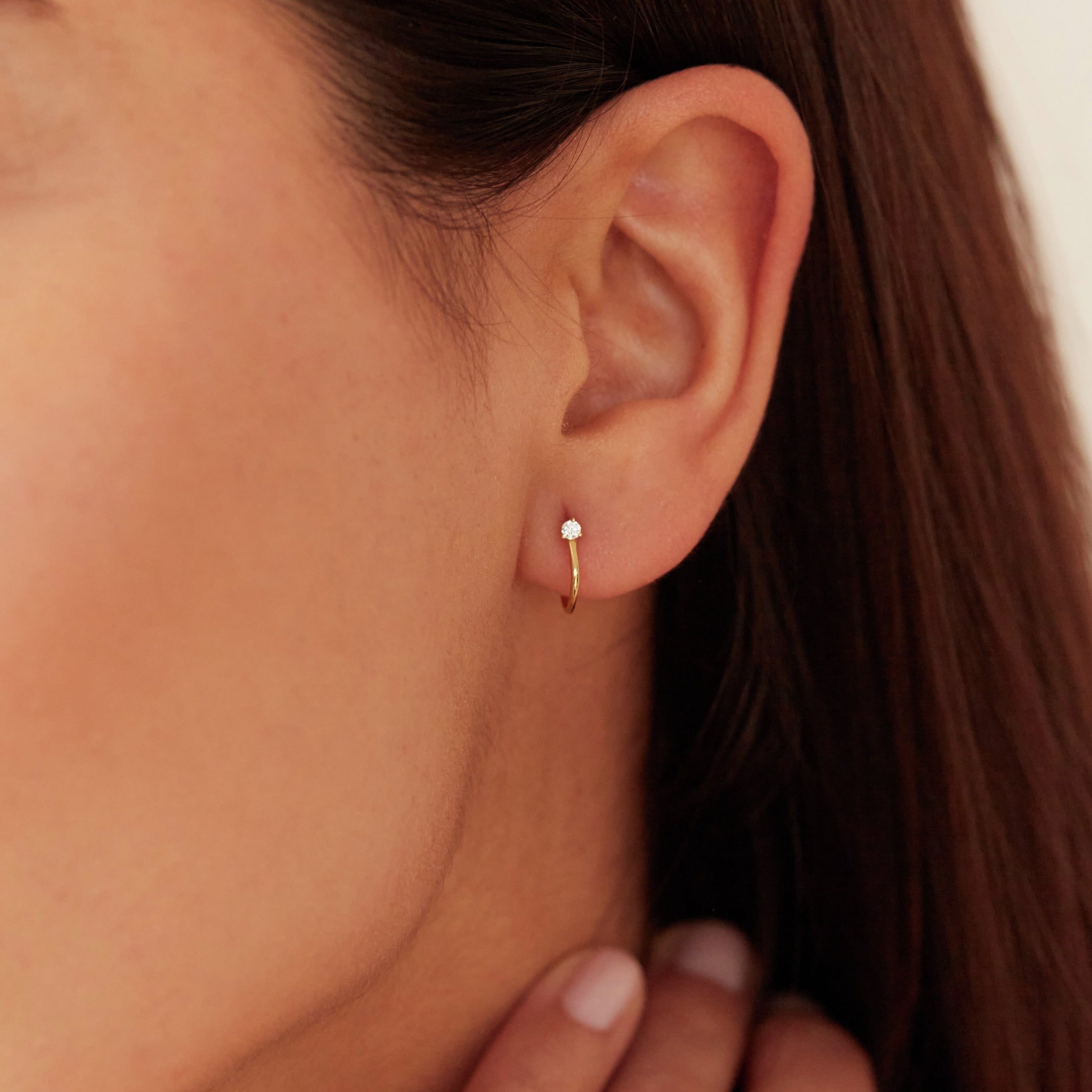 A gold diamond style lobe hoop stud earring in one ear lobe