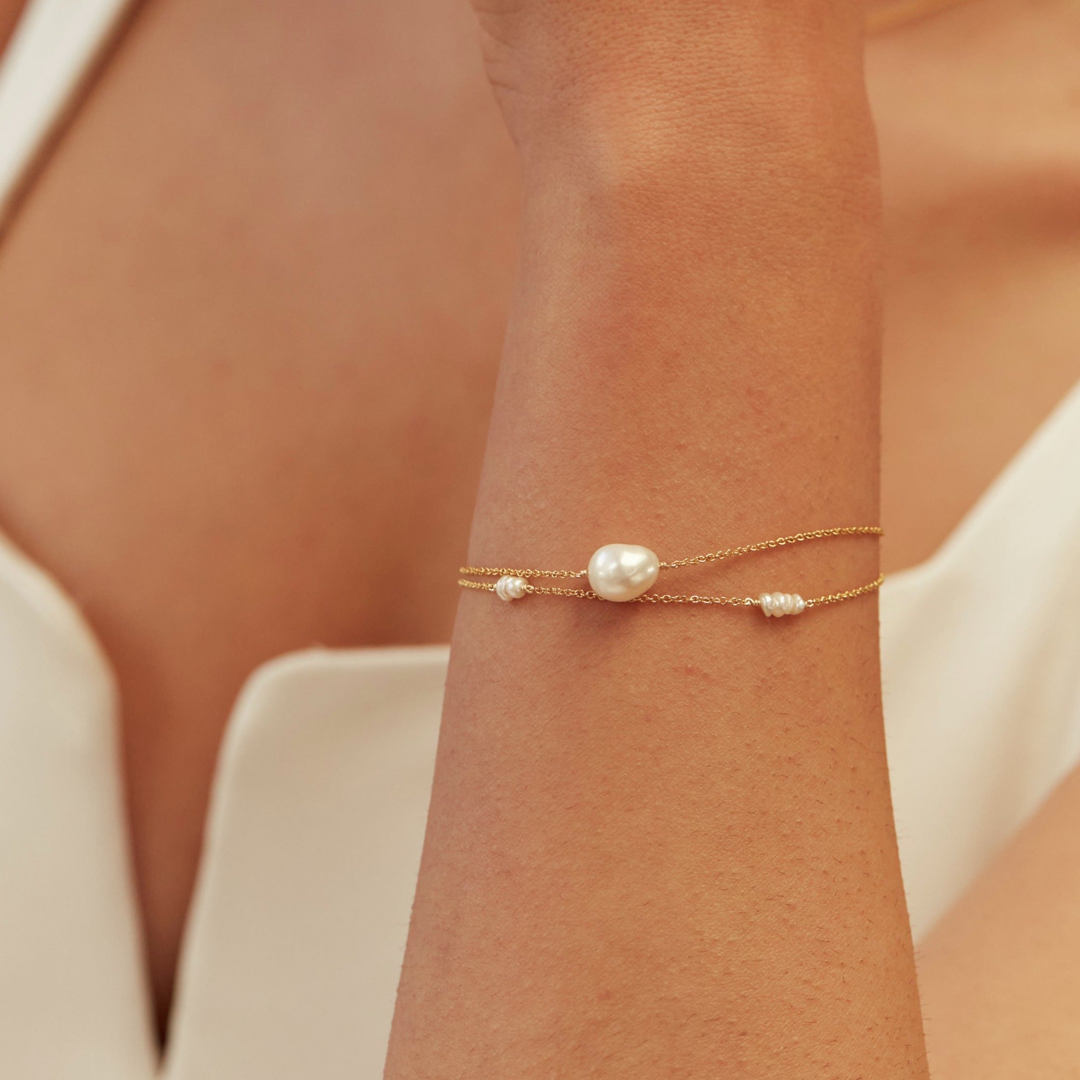 Gold large pearl bracelet layered with a pearl bracelet on a wrist 