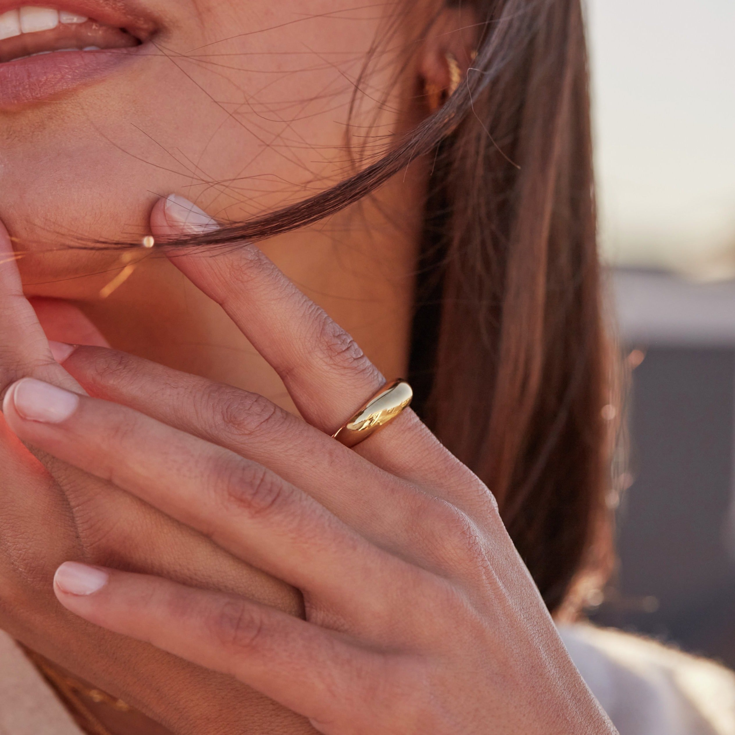 Gold plain dome ring on the finger of a brunette woman touching her face looking to the side