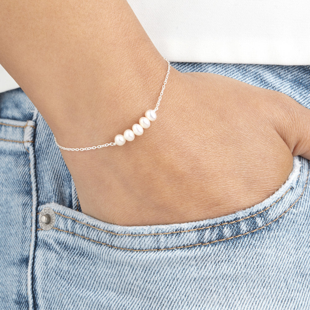 Silver cluster pearl bracelet around a wrist with the hand in a denim pocket