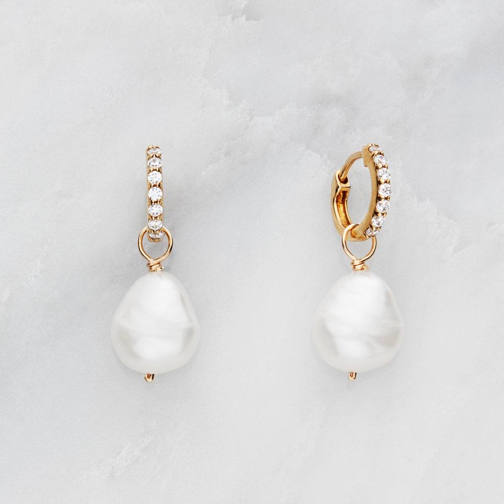 Gold huggie pearl drop earrings on a marble background