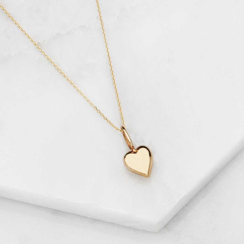 Gold heart pendant necklace on marble surfaces