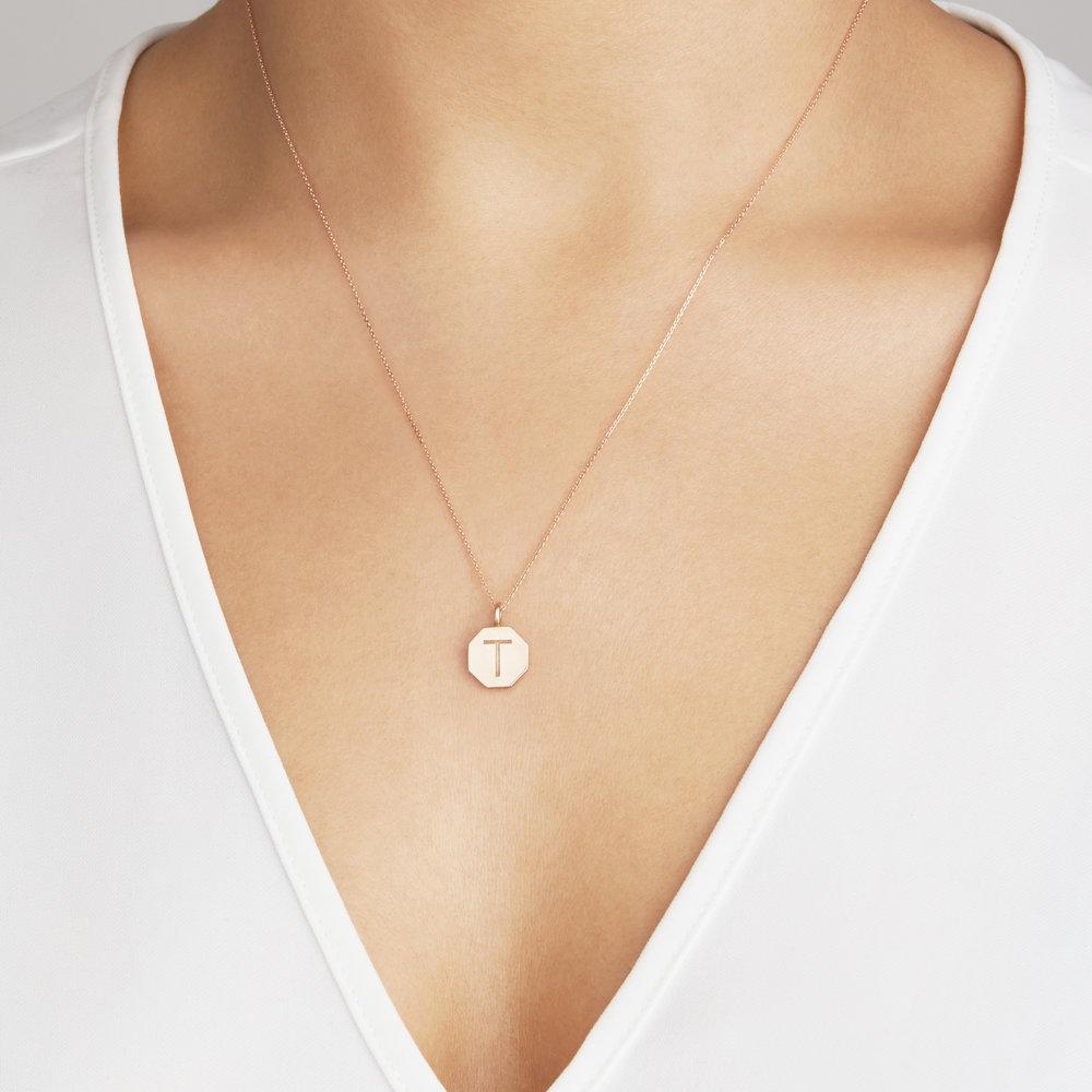 Gold personalised hexagon necklace with the letter 'T' engraved on it around a neck with a white v neck top