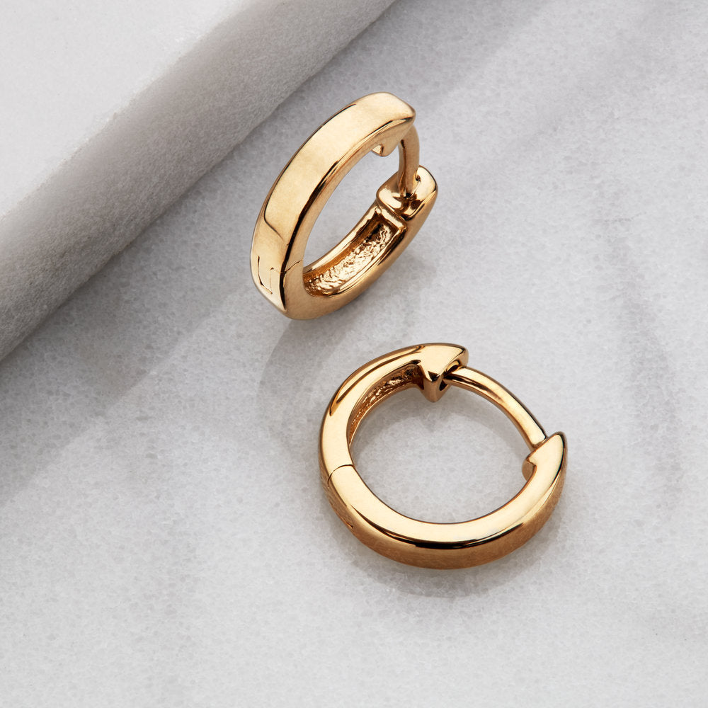 Gold plain huggie hoop earrings on a marble surface