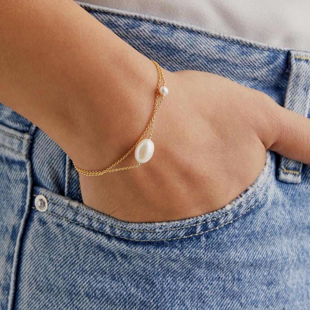 Gold layered large and small pearl bracelet on wrist with hand in blue jean pocket