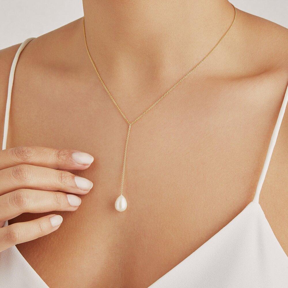 Gold large pearl lariat necklace around a neck with a white top