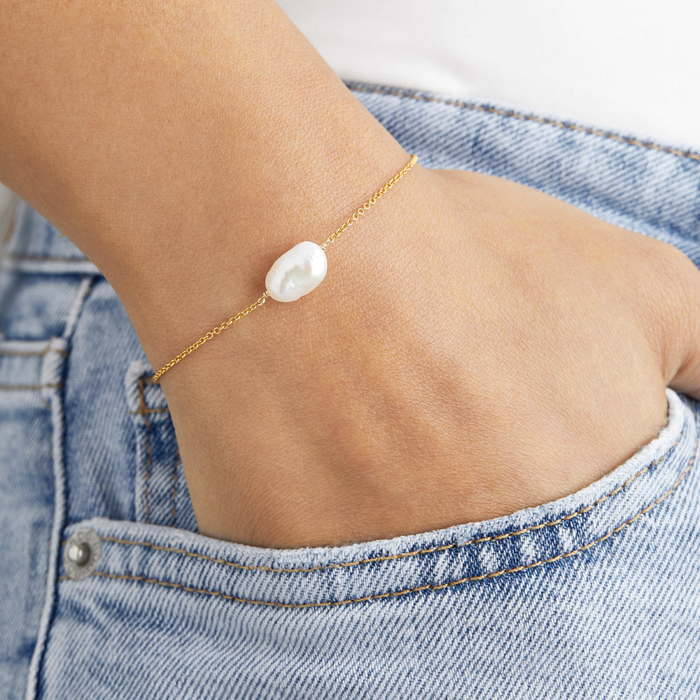 Gold large pearl bracelet on a wrist with hand in blue jean pocket