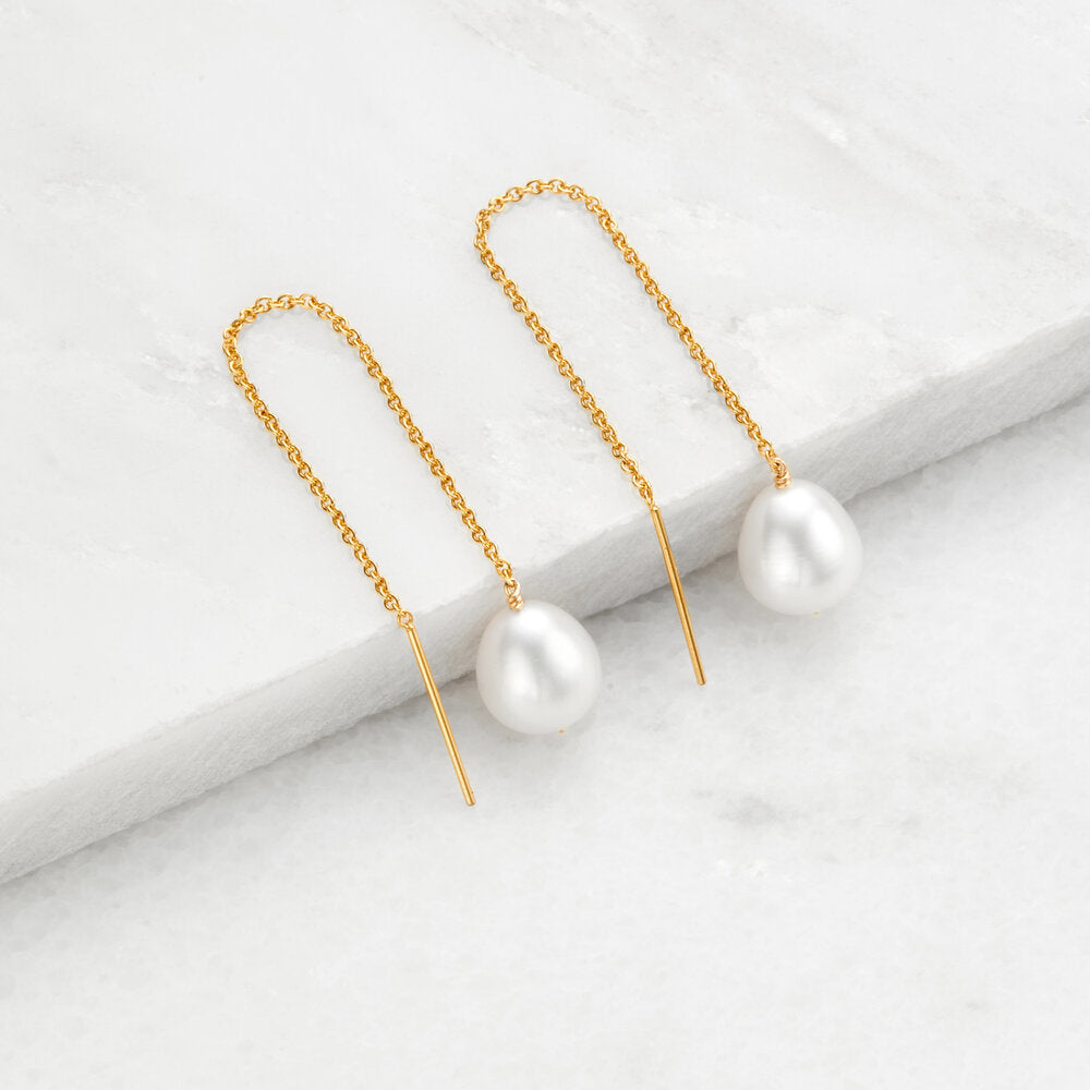 Gold large pearl drop ear threaders on marble surfaces 