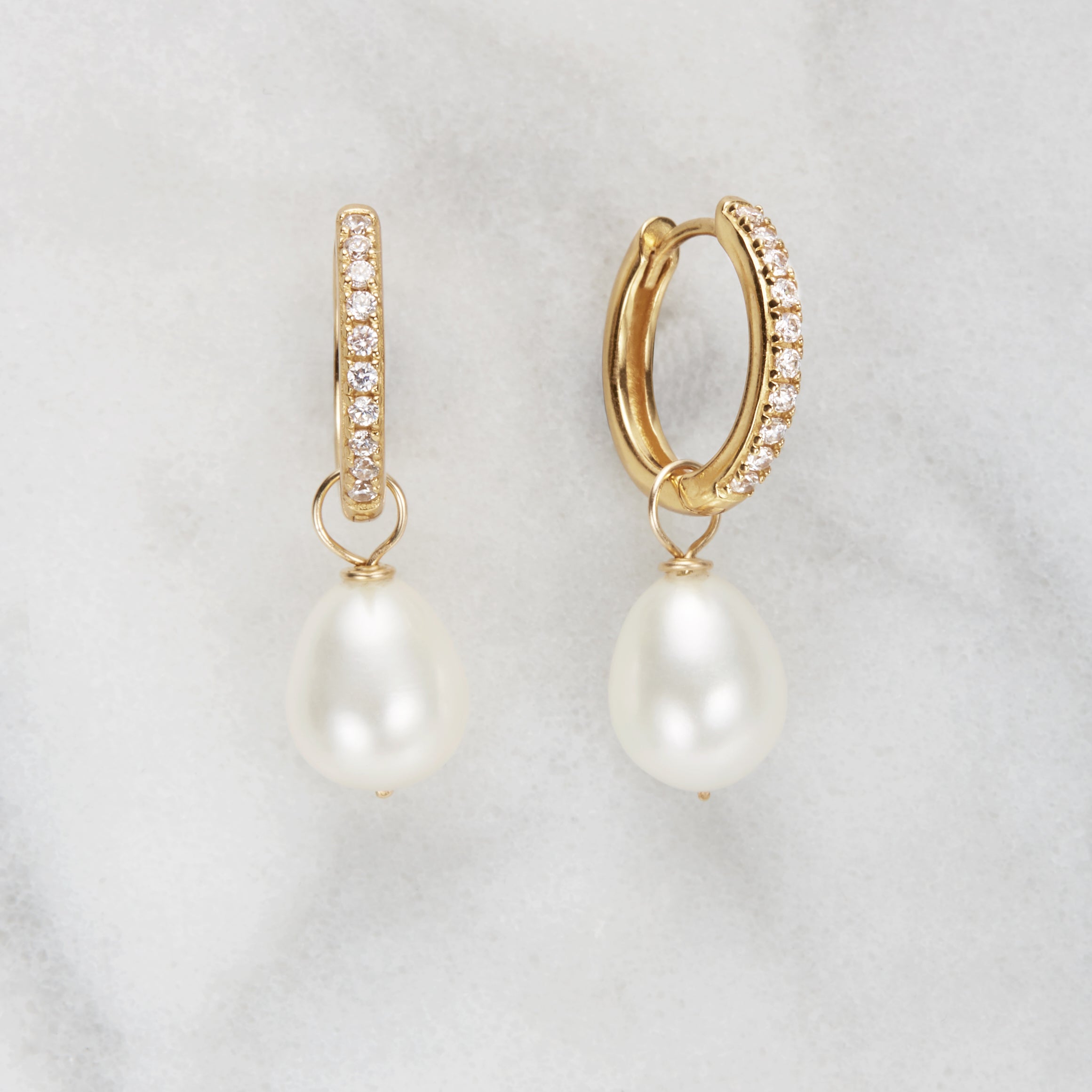 Gold diamond style large pearl drop hoop earrings on a marble background
