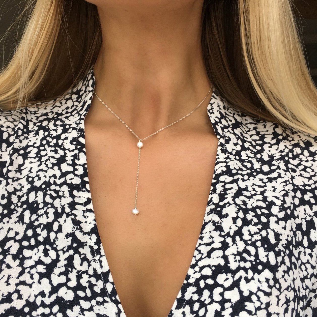 Gold pearl lariat necklace around the neck of a blonde woman wearing a black shirt with white spots