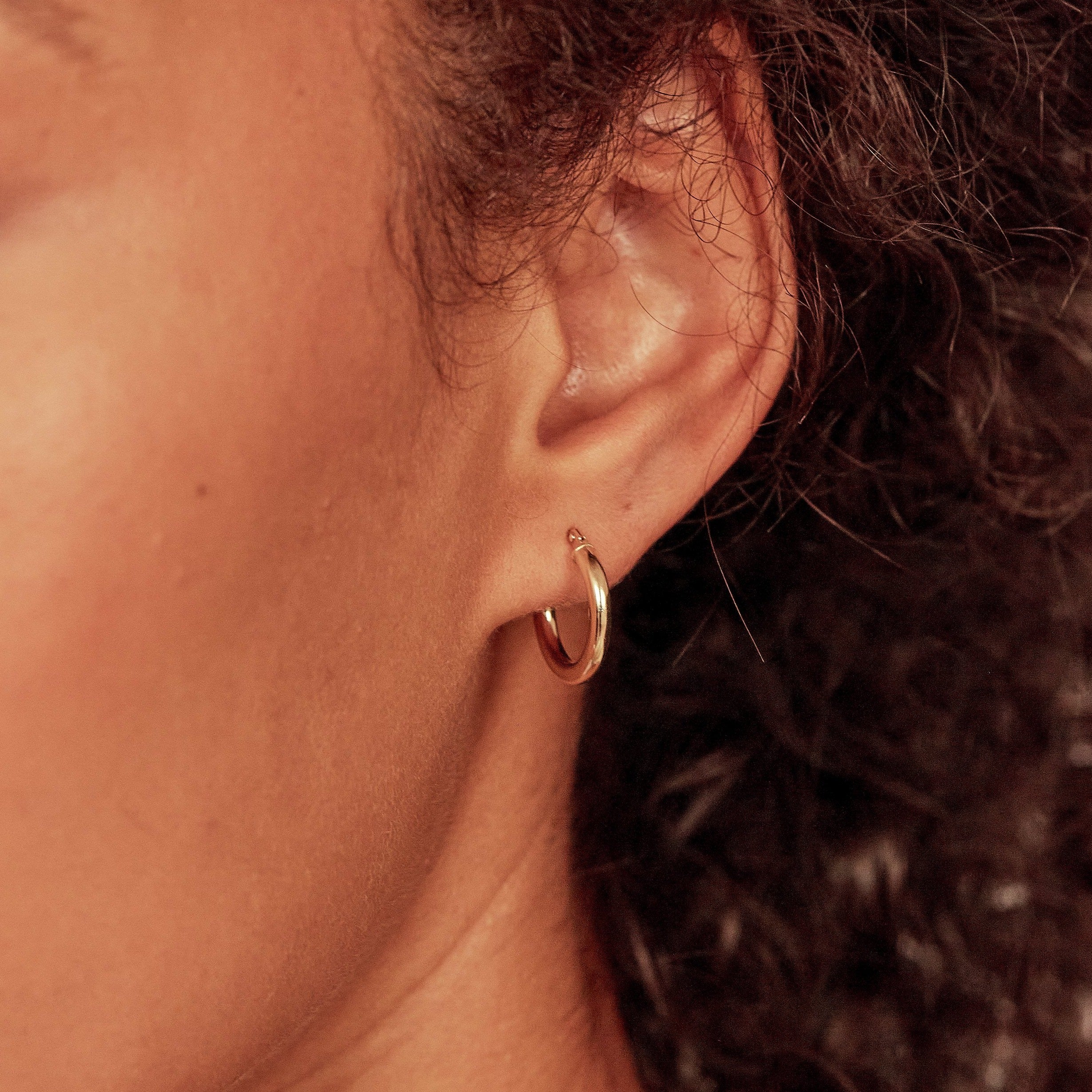 Gold small rounded hoop earring in one ear lobe