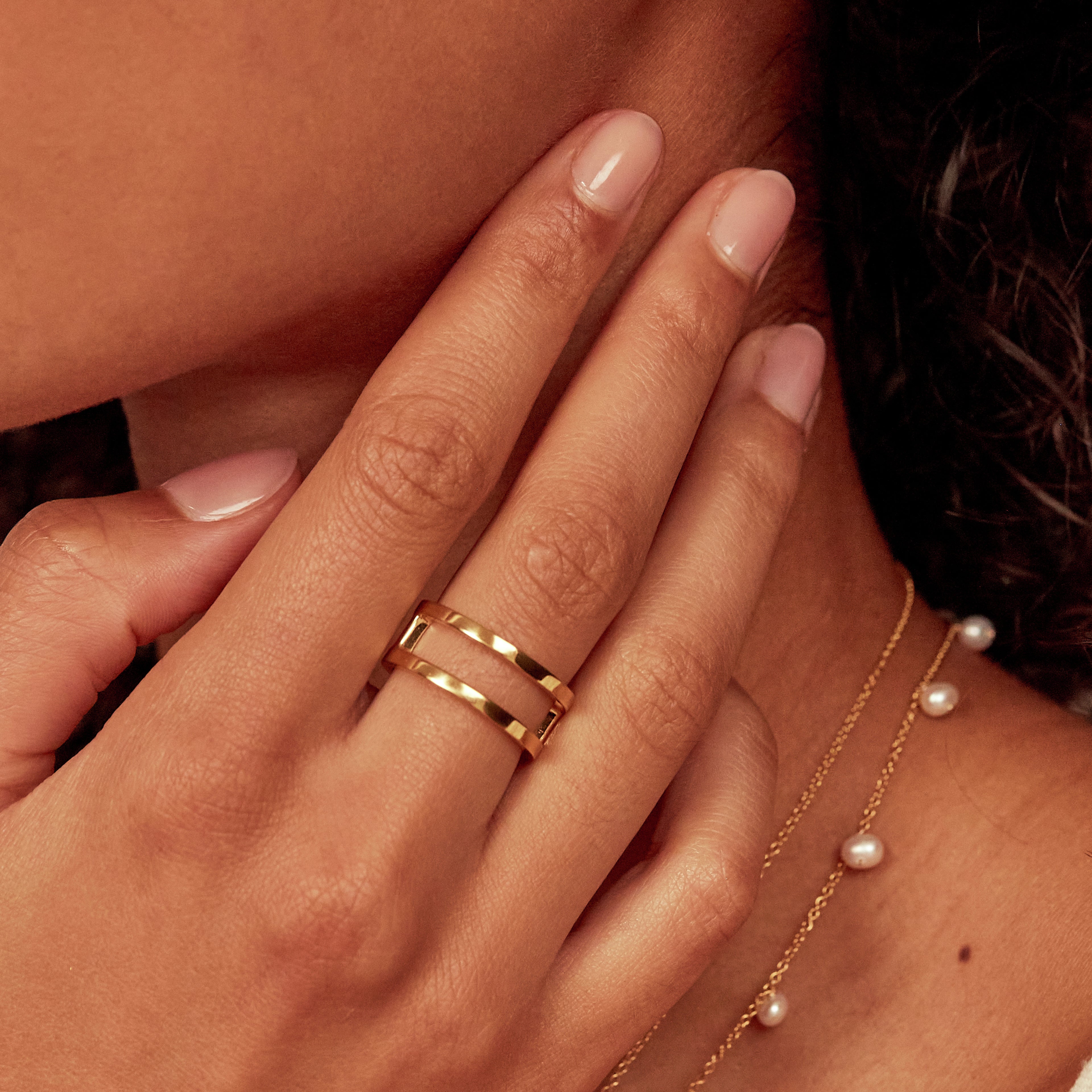 Gold double band ring on a hand with a pearl necklace