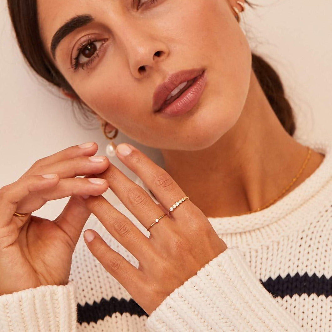 Gold graduated diamond style stacking ring on a finger with gold thin diamond style stacking ring  on a another finger of a brunette woman wearing a striped cream and black jumper