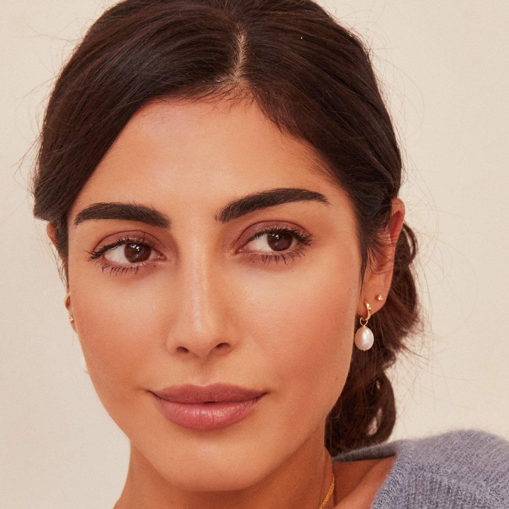 Brunette woman wearing a pearl earring and a gold small diamond stud in one ear lobe