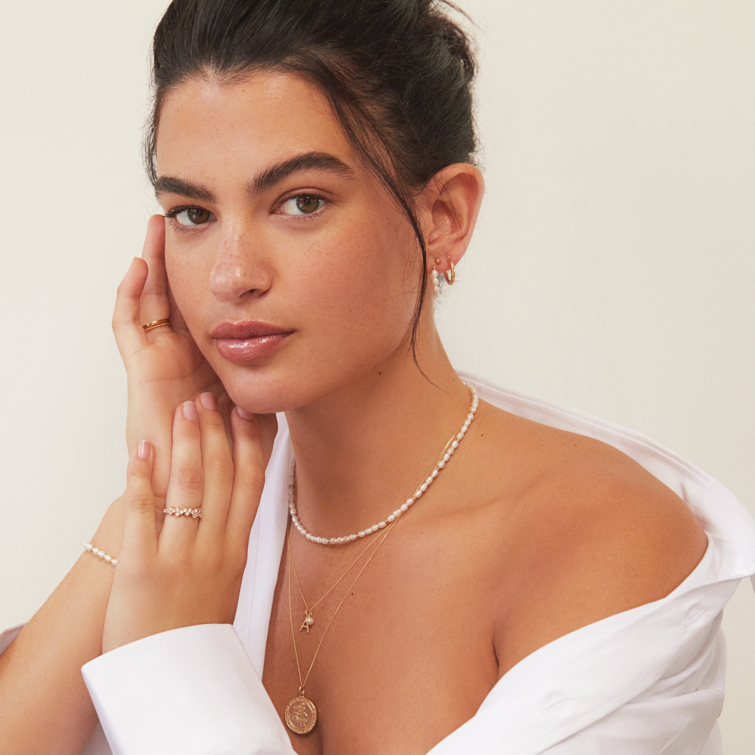 Gold beaded seed pearl choker on a brunette woman layered with gold necklaces and also wearing gold earrings and rings