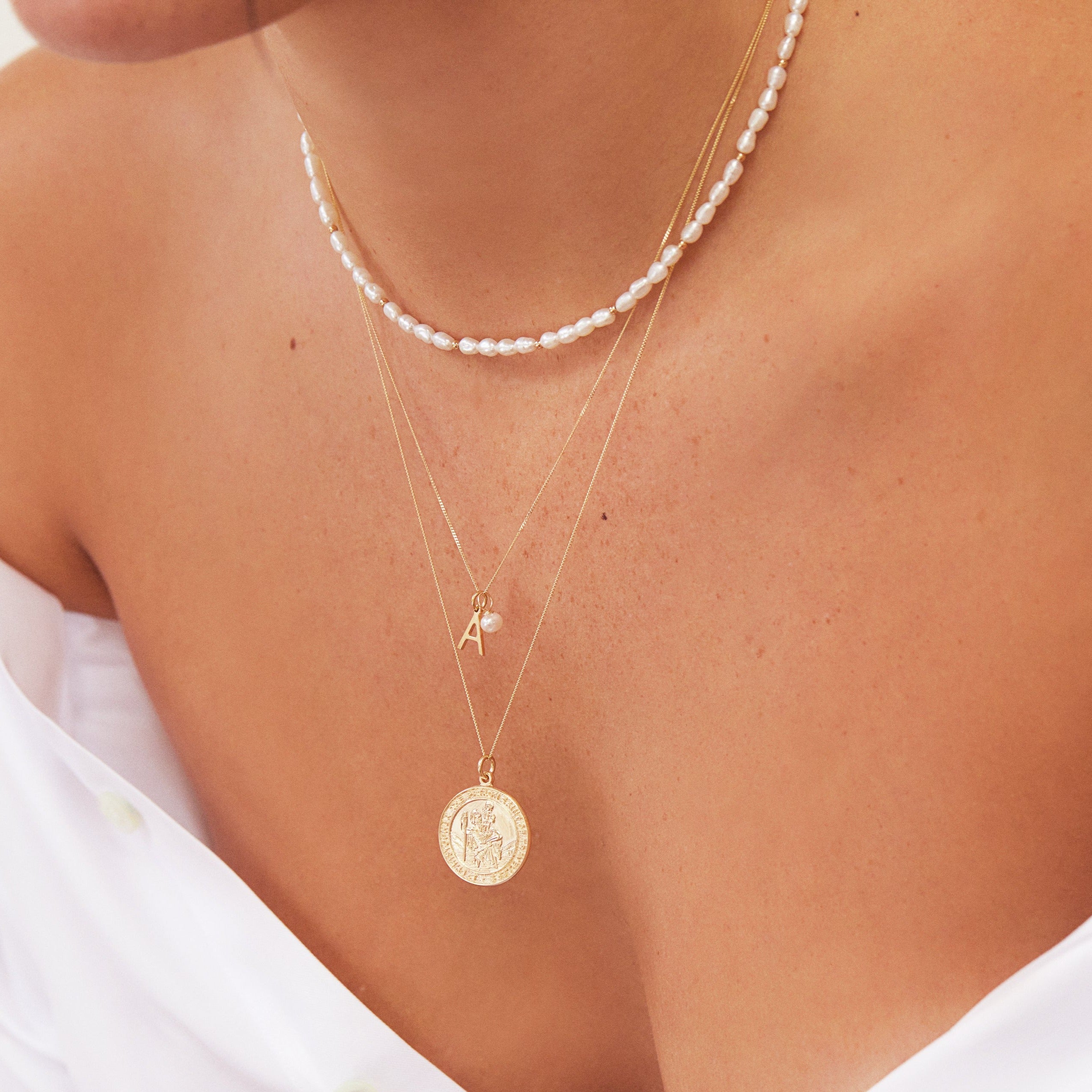Gold beaded seed pearl choker layered with an A letter gold necklace and a gold symbol necklace around the neck