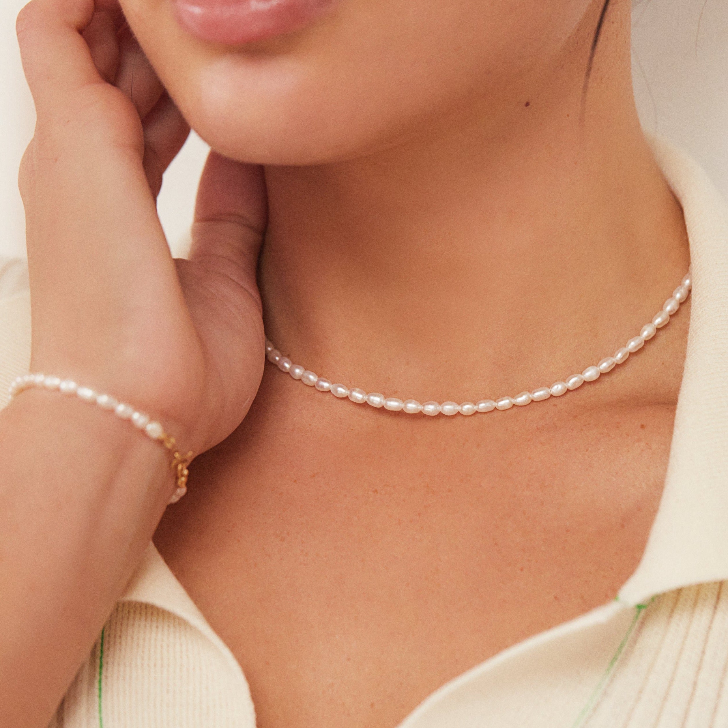 Gold seed pearl choker around a neck with a gold seed pearl bracelet around a wrist
