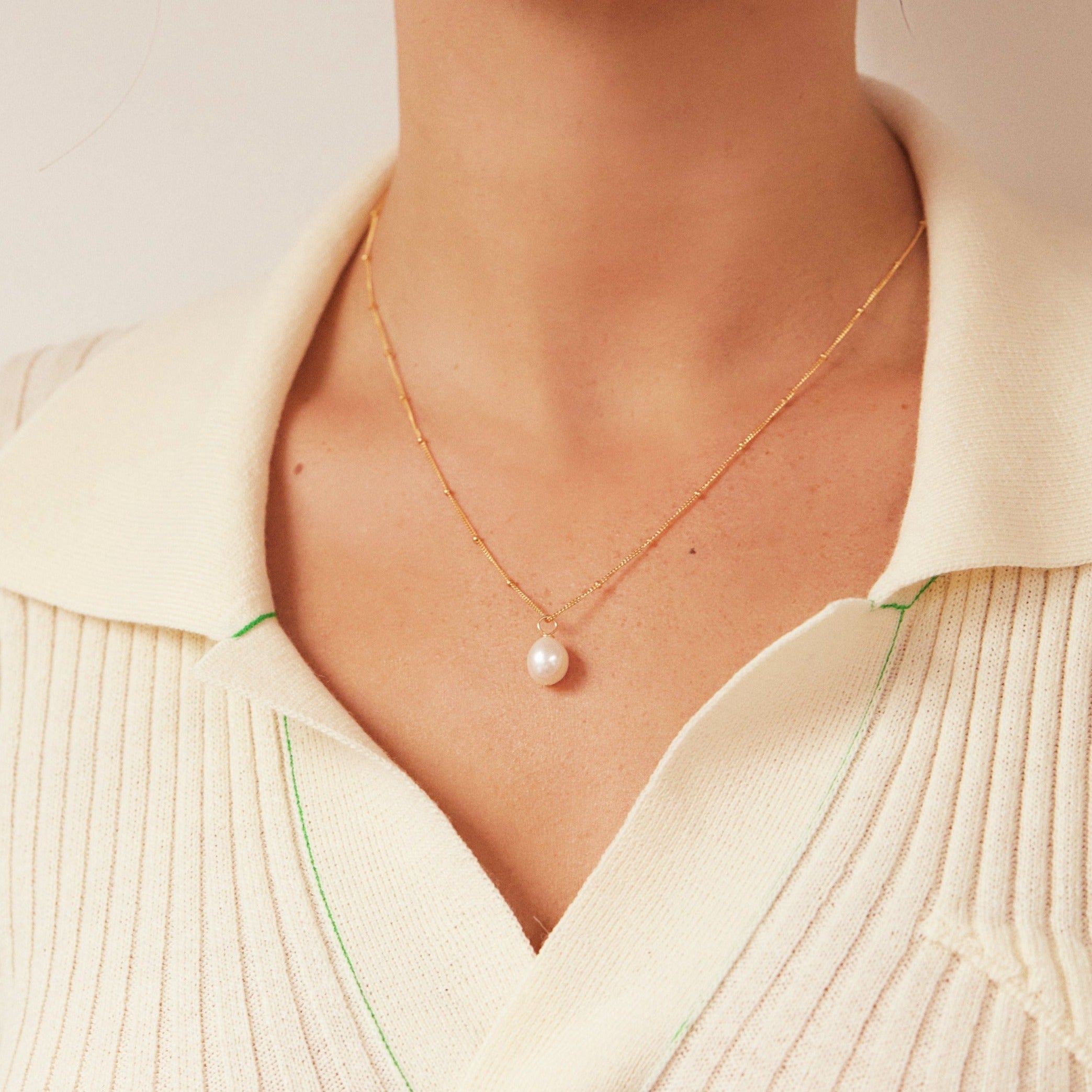 Gold large pearl satellite necklace on a woman with a cream collared shirt