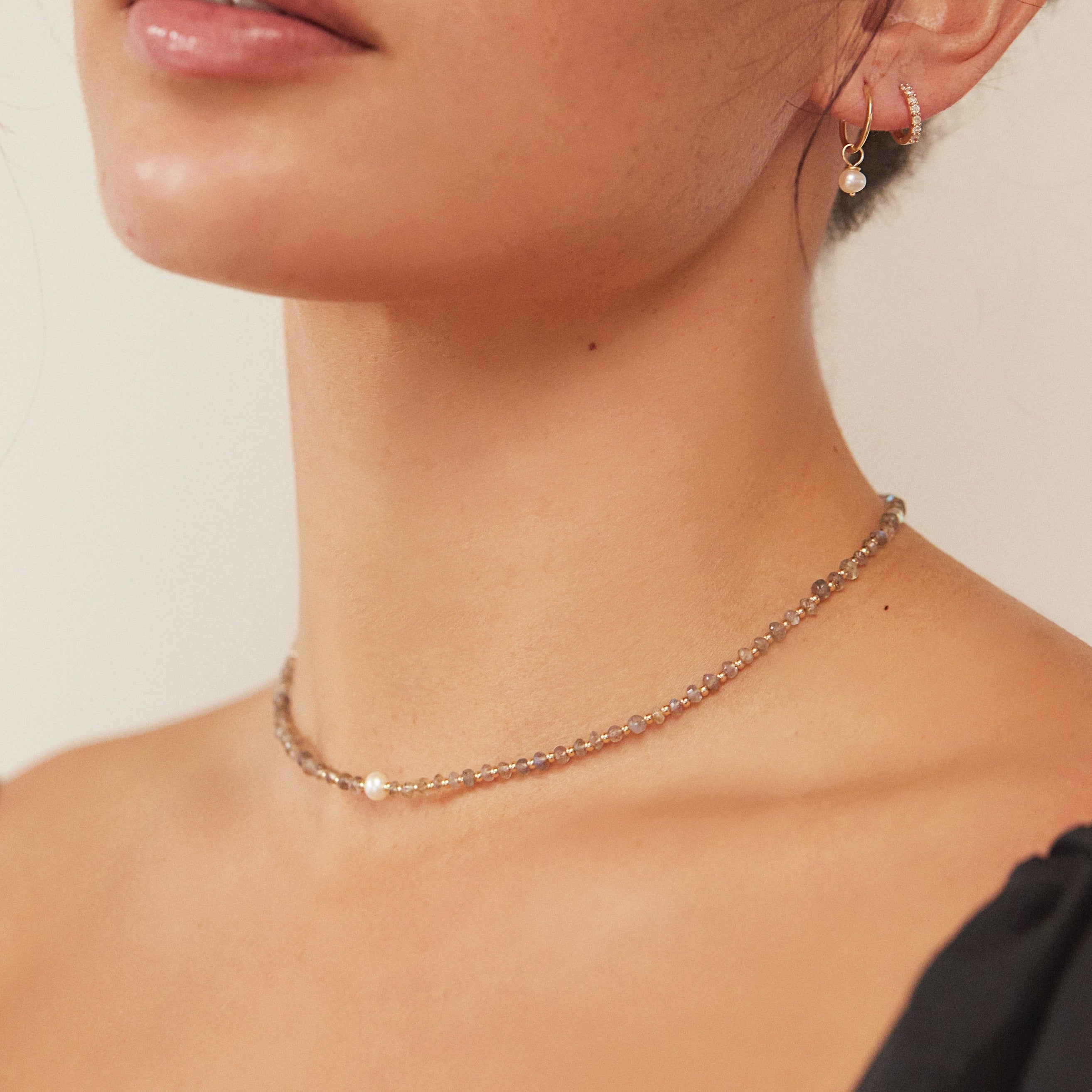Gold labradorite gemstone choker around a neck with a pearl earring and diamond style earring in one ear lobe