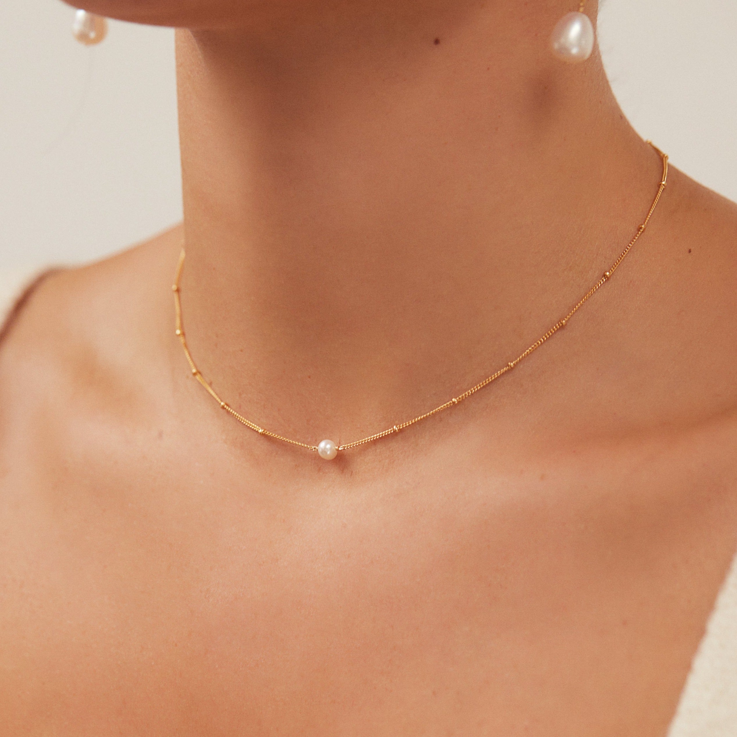 Gold satellite single pearl choker around a neck