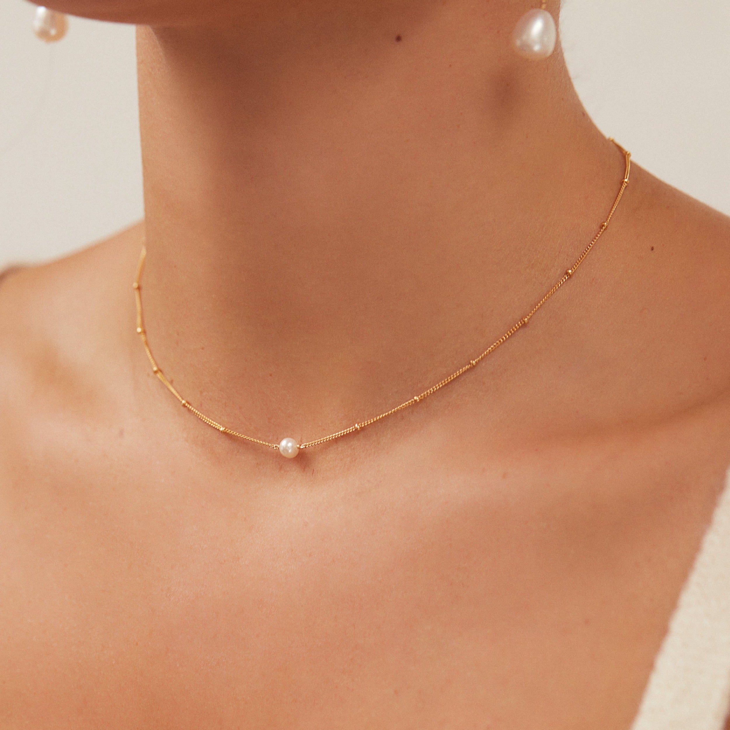 Gold satellite single pearl choker around a neck of a woman also wearing pearl earrings