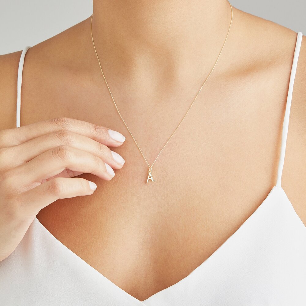 Solid gold curve initial letter necklace 'A' around the neck of a woman wearing a white strappy top