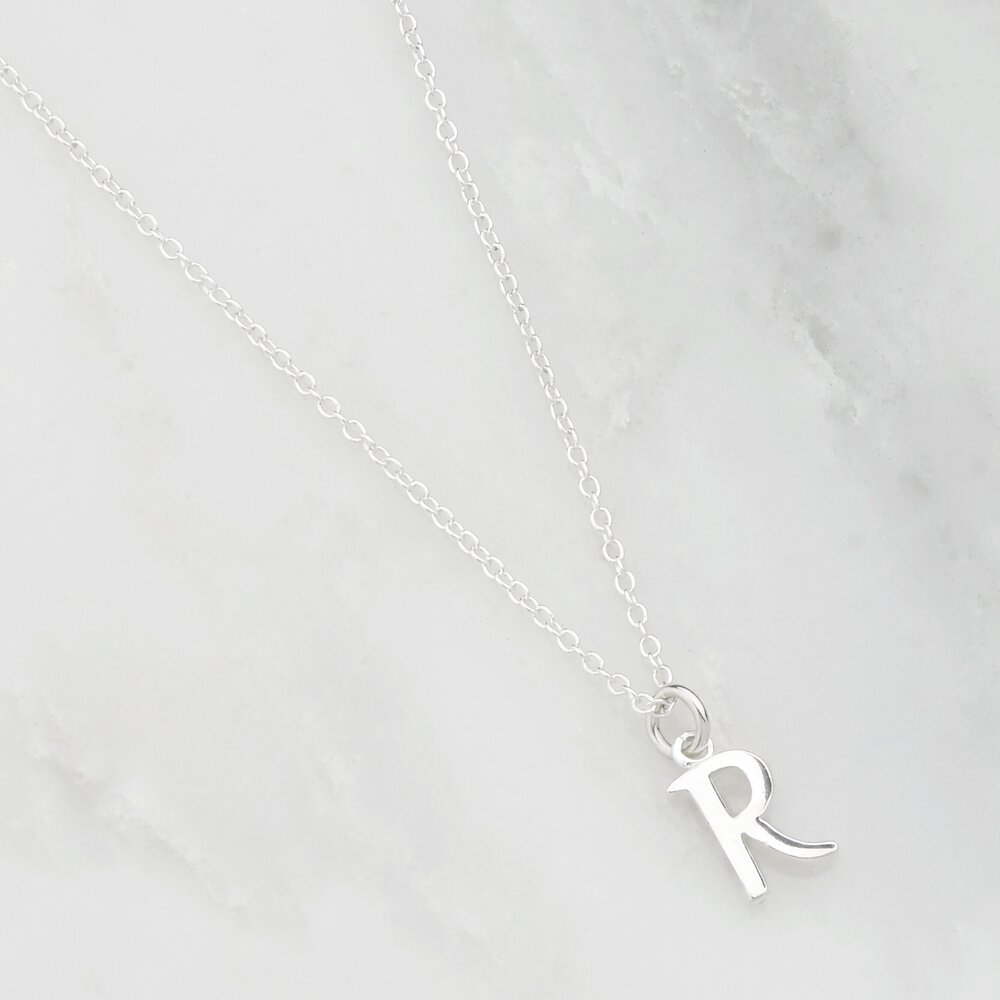 Silver curve initial letter necklace 'R' on a marble surface