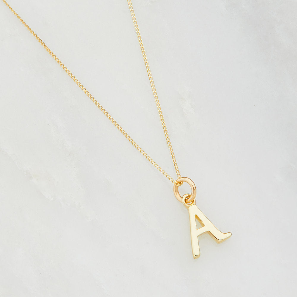 Solid gold curve initial letter necklace 'A' on a marble surface
