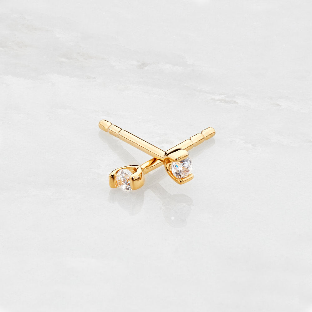 Gold small diamond style studs one crossed on top of the other on a marble surface
