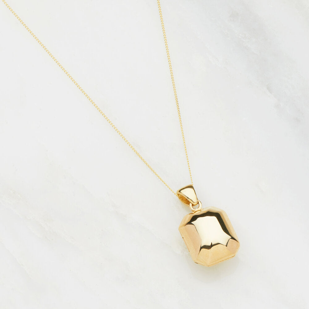 Solid gold ball locket laying on a white surface