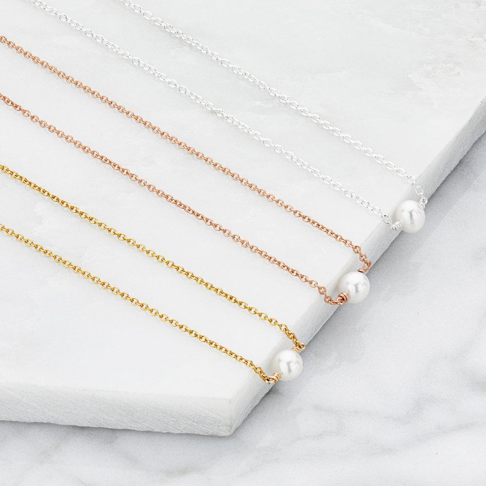 A gold single pearl choker, rose gold single pearl choker and silver single peal choker placed in a row next to one another on a marble ledge 