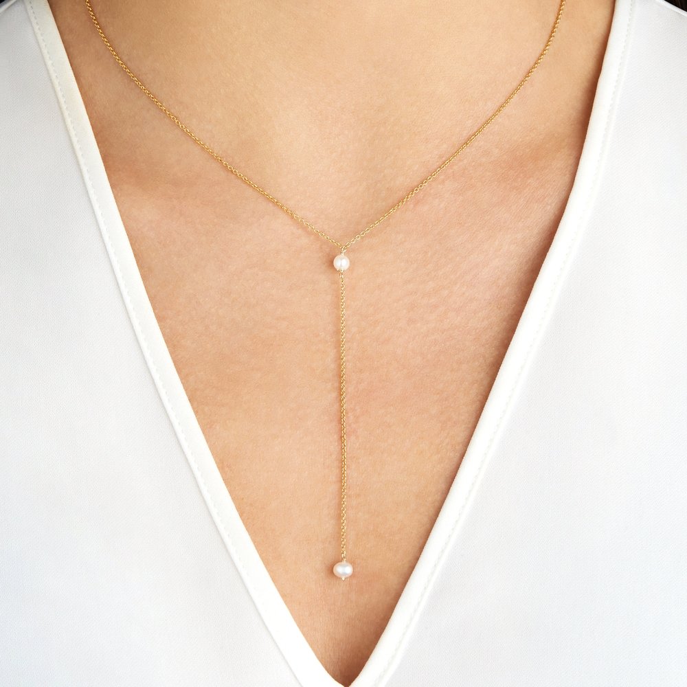Gold pearl lariat necklace around a neck with a white v neck top
