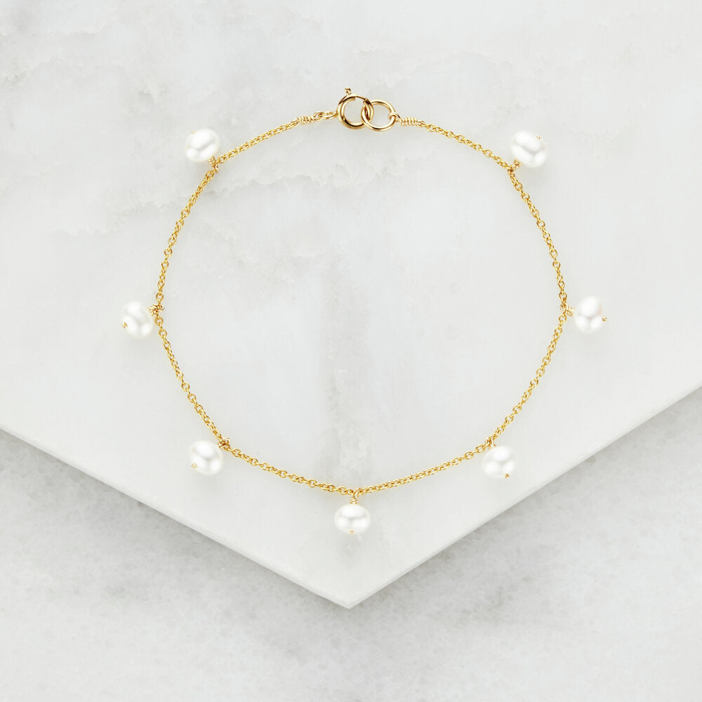 Gold pearl drop bracelet on marble surfaces