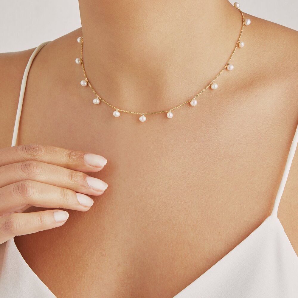 Gold pearl drop choker around a neck with a white top