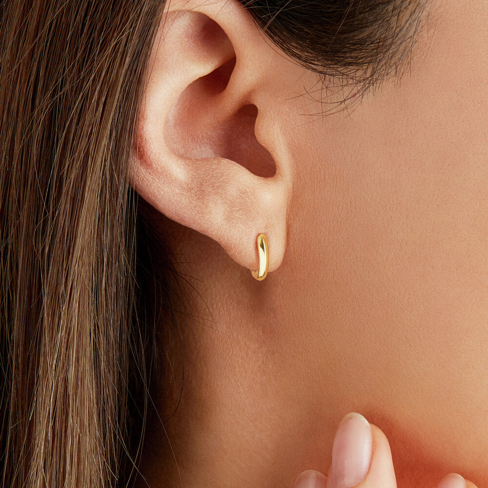 Close up of gold small rounded plain huggie hoop earring in an ear lobe