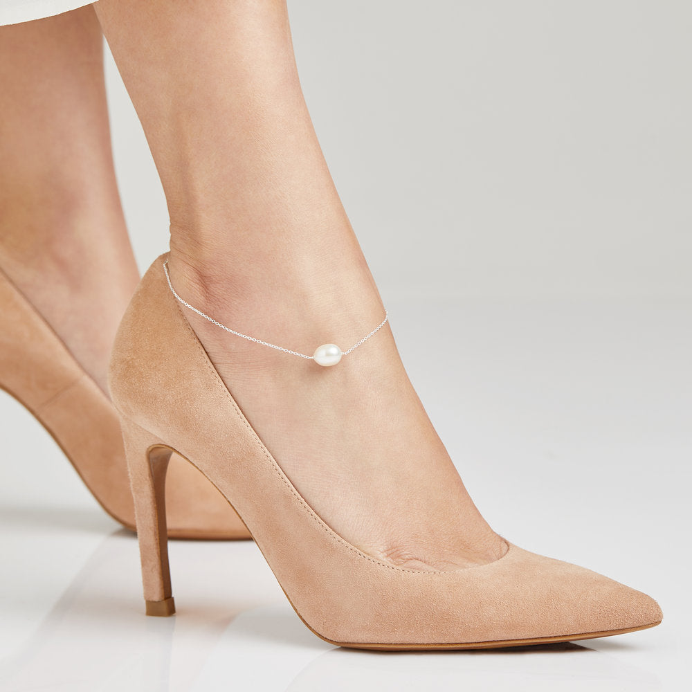 Gold large pearl anklet worn around an ankle with beige heels